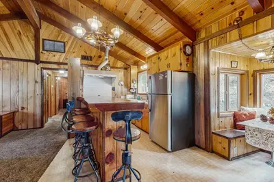a kitchen with a refrigerator and a counter with stools at Idle Ours Cabin ~ Rustic and Cozy Cabin with Fireplace & Private BBQ - Walk to Big Bear Lake in Fawnskin