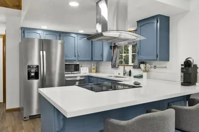 a kitchen with blue cabinets and a stainless steel refrigerator at The Fox Den Big Bear ~ Modern Mountain View Retreat w/ Hot Tub in Big Bear City