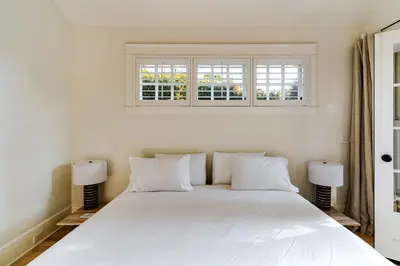 a white bed in a bedroom with two windows at Venice 2BR and Guest Studio with Tub & Garden in Los Angeles