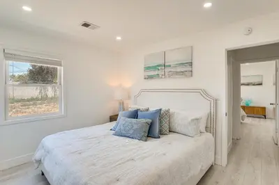 a white bedroom with a large bed with blue pillows at 7 Mi Huntington Beach Family Home with Patio! in Midway City