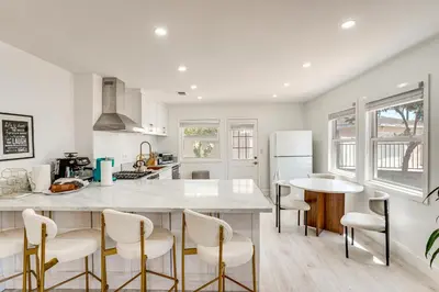a kitchen with a large white counter and chairs at 7 Mi Huntington Beach Family Home with Patio! in Midway City