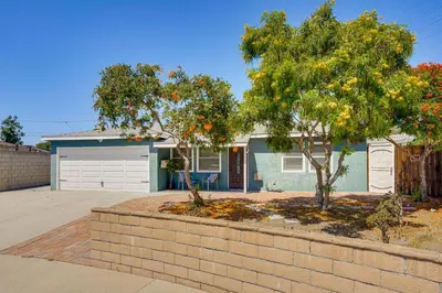 a house with a tree and a brick wall at 7 Mi Huntington Beach Family Home with Patio! in Midway City