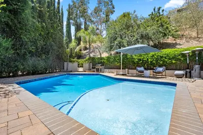 a swimming pool with an umbrella and chairs at Hillside Modern Retreat with pool BBQ and MORE in Los Angeles