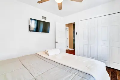 a white bedroom with a bed and a tv on the wall at Modern Pool house with hot tub and relaxing backyard in Long Beach