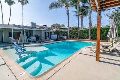 a swimming pool with chairs and umbrellas next to a house at Modern Pool house with hot tub and relaxing backyard in Long Beach