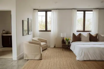 a bedroom with a bed and a chair and windows at Dreamy Mid-Century Modern Pad in Los Angeles