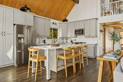 a kitchen with white cabinets and a island with bar stools at The Crown A-Frame Gated Central AC Lake Access in Lake Arrowhead