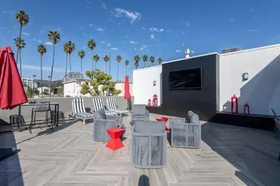 a rooftop patio with chairs and a television and palm trees at Hollywood Stars 2 Bedroom Apartment in Los Angeles