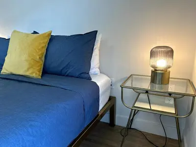 a bed with a blue blanket and a glass table with a lamp at Cozy studio in heart of Santa Monica free parking in Los Angeles