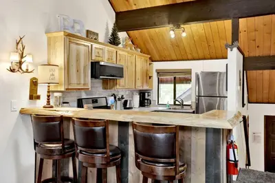 a kitchen with wooden cabinets and a counter with bar stools at Switzerland Summit Condo- Cozy Base Camp Resort Chalet- Walk to Ski Lifts + Hiking in Big Bear Lake