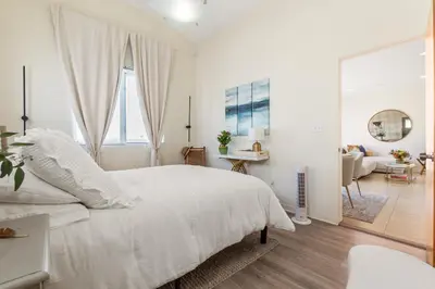 a white bedroom with a white bed and a living room at Ocean View condo in the heart of Manhattan Beach in Manhattan Beach