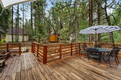 a wooden deck with a table and chairs and an umbrella at Navigate Stays 5BR Group Lodge Near Mountain & Fun in Big Bear Lake