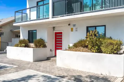 a white building with a red door and some plants at 3BR Urban Retreat with Modern Amenities in Los Angeles