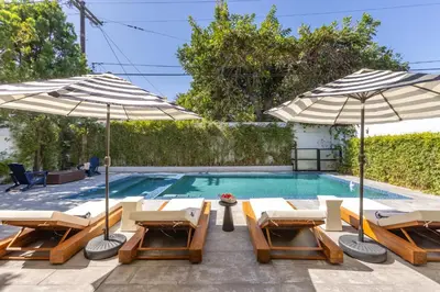 a swimming pool with two umbrellas and lounge chairs and a swimming pool at 5BR Modern West Hollywood Retreat in Los Angeles
