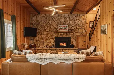a living room with a stone wall with a fireplace at Lakeside Lodge - Deck Views, Golf, Basketball, Spa in Fawnskin