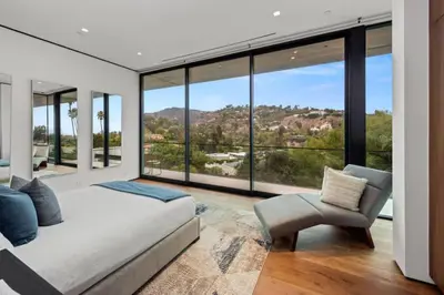 a bedroom with a bed and a chair and large windows at Luxurious 5BR Villa in BH with Pool, Theater, and Views in Los Angeles