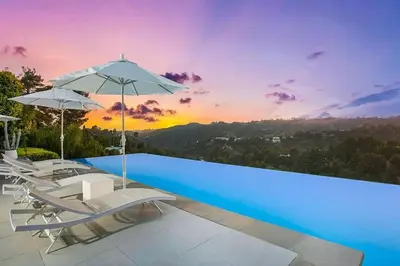 a pool with chairs and umbrellas with a sunset at Beverly Hills Mansion W. Stunning Views in Beverly Hills
