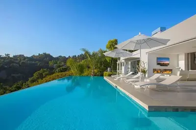 a swimming pool with chairs and umbrellas next to a house at Beverly Hills Mansion W. Stunning Views in Beverly Hills