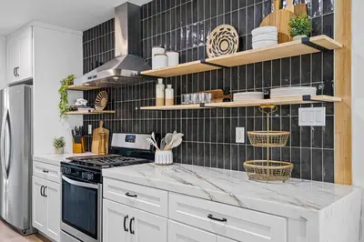 a kitchen with white cabinets and a black tiled wall at Pool House Retreat near LAX, SoFi & Beach in Inglewood