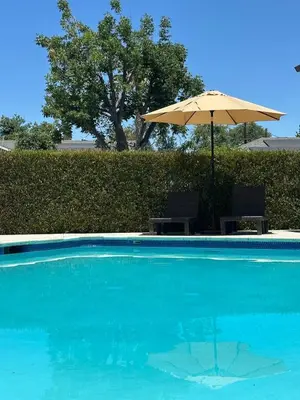 an umbrella and chairs next to a swimming pool at Modern 3BR with King Bed, Gated Pool and BBQ Oasis in West Valley Area Heliport