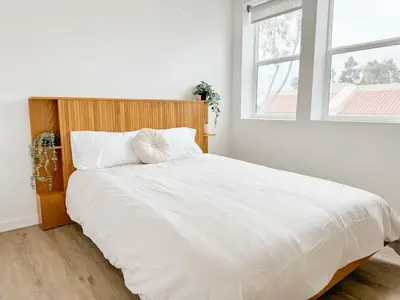 a bedroom with a large white bed with a wooden headboard at Central, Urban Townhouse with Private Roof Deck in Garden Grove