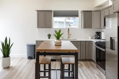 a kitchen with gray cabinets and a table with stools at The Harvard Modern Retreat LA in Los Angeles