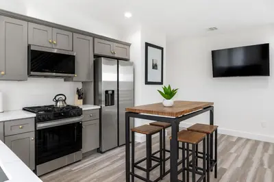 a kitchen with stainless steel appliances and a table with stools at The Harvard Modern Retreat LA in Los Angeles