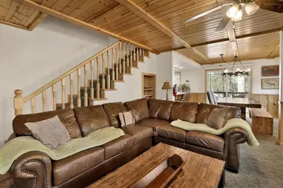 a living room with a brown leather couch and stairs at Brownie Resort Your Walk-to-Summit Getaway Family's Snowboarders Skiers in Big Bear Lake