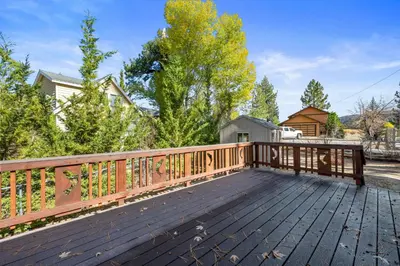 a large deck with a wooden railing and trees at Log Cabin Dream - Log Cabin, Walk to Lake, Fireplace, Deck, BBQ in Big Bear Lake