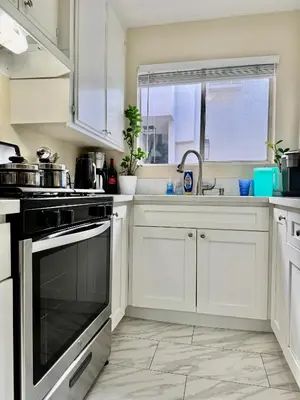 a kitchen with white cabinets and a stove top oven at Proper Stays at Melrose - West Hollywood Modern 3-Bedroom Designer Home in Los Angeles
