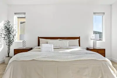a white bedroom with a large bed and two windows at Luxury Mountain View Home w/ large backyard in Santa Clarita