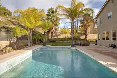a swimming pool in front of a house with palm trees at Mountain View Home with Pool & Fenced-In Yard in Santa Clarita
