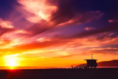 a sunset on the beach with a lifeguard tower at 2 King Beds DTSM! Walk to Pier, Promenade & Beach in Los Angeles