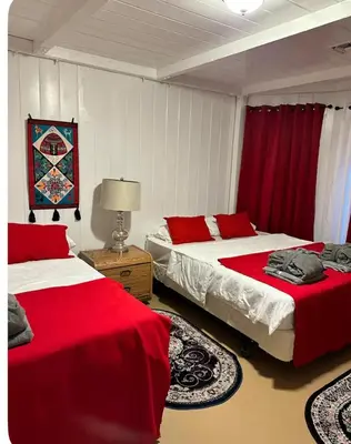a bedroom with two beds with red sheets and a rug at Naryn Guest House 3 in Los Angeles