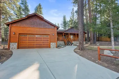a house with a garage in the woods at Pine Cottage - NEW! Shuffleboard, Pool Table, Smart TVs, Fenced Yard in Big Bear Lake