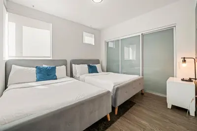 two beds in a white room with blue pillows at Heart of Santa Monica Chic Condo in Los Angeles