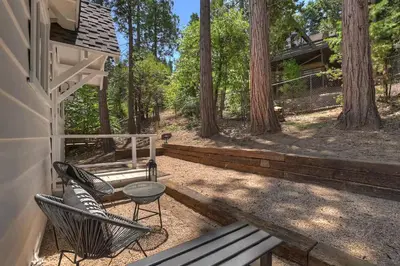 a patio with two chairs and a table in the woods at Yama Cabin - 5 min walk to the village, EV plug, hot tub, kid & pet friendly in Lake Arrowhead