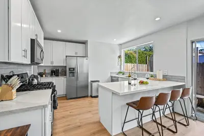 a kitchen with white cabinets and a kitchen island with bar stools at Belmont Shore Getaway with Hot Tub and Firepit in Long Beach