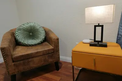 a brown chair with a green pillow sitting next to a table at Modern Oasis Studio - near LAX, SoFi, USC, DTLA in Los Angeles