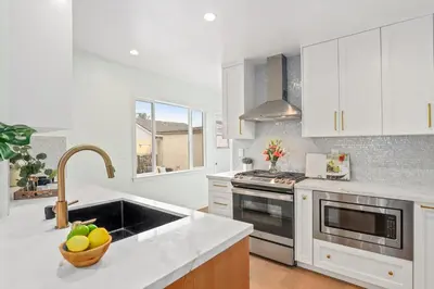a kitchen with white cabinets and a sink with a bowl of fruit at Quintessential SoCal indoor outdoor living with POOL in Long Beach