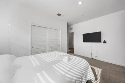 a white bedroom with a bed and a flat screen tv at Serenity House- Newly Built, Peaceful Stay in Bakersfield