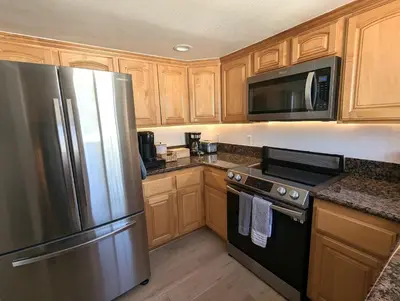 a kitchen with wooden cabinets and a stainless steel refrigerator at Walk 2min to BEACH! Boho 3-Bedroom BEACH Pad with AC, Patio, Laundry & Mid Size Parking in Long Beach