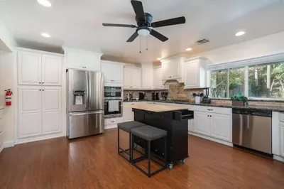 a kitchen with white cabinets and a ceiling fan at Your Poolside Hideaway in Bakersfield