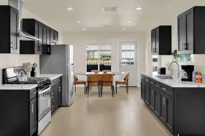 a kitchen with black cabinets and a table with chairs at Stylish LA Retreat Near Disney Knotts SoFi in Paramount