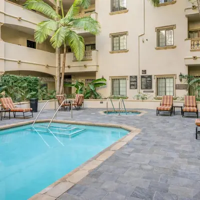 a pool in front of a building with chairs and a palm tree at Evera Residence- 1Bed with Free Parking, Pool and Sauna in Los Angeles