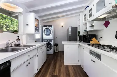 a kitchen with white cabinets and a washer and dryer at SoCal Retreat with Pool and Spacious Backyard in Canoga Park