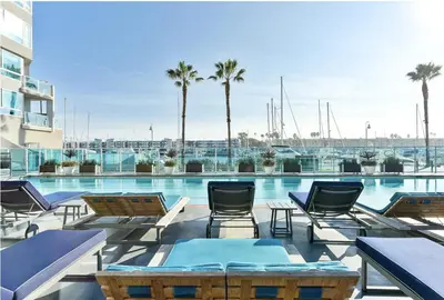 a patio with chairs and a swimming pool with palm trees at The Zenith Penthouse - Ocean Panoramas & Salt Air in Los Angeles