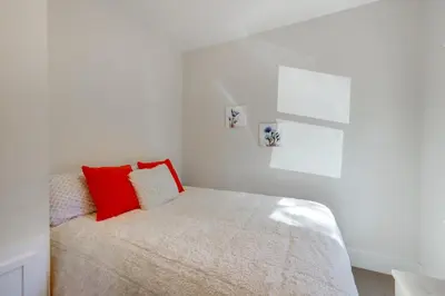 a white bedroom with a bed with red pillows at Walk to Lake Arrowhead Village Bright Gem with Deck in Lake Arrowhead