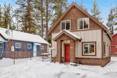 a house with a red door in the snow at Ursa Major Lodge | Walk to Lake & Village | Pet Friendly Retreat in Big Bear Lake