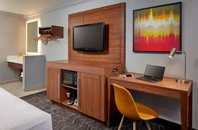 a hotel room with a desk with a laptop and a television at Studio Inn & Suites at Promenade Downey in Downey